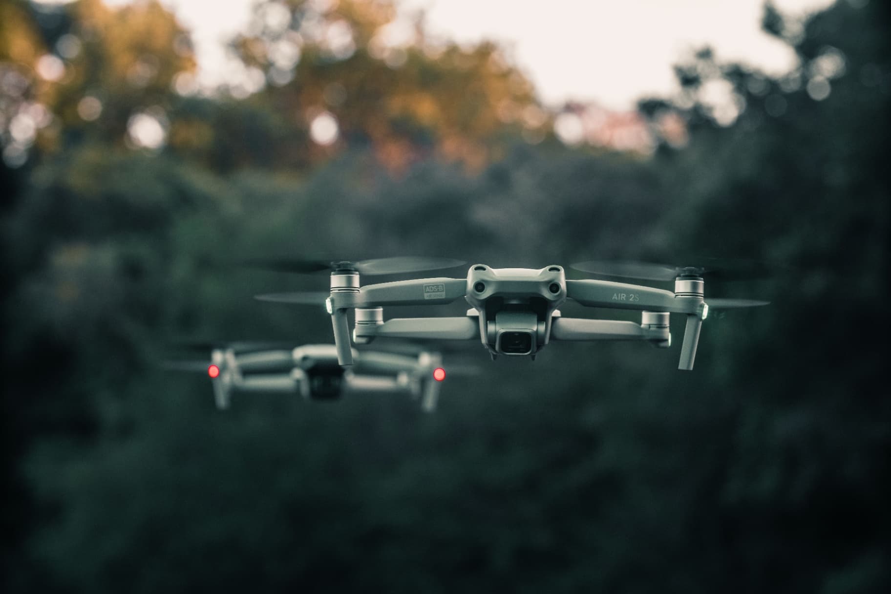 Dva drony DJI Air 2S vznášajúce sa nad lesom pri západe slnka